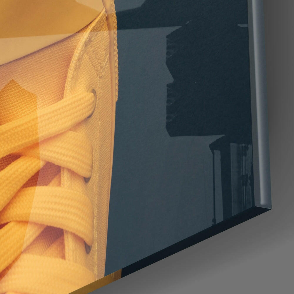 Close-up side view of glass art panel showing yellow laces on textured fabric with dark silhouette visible through glass.