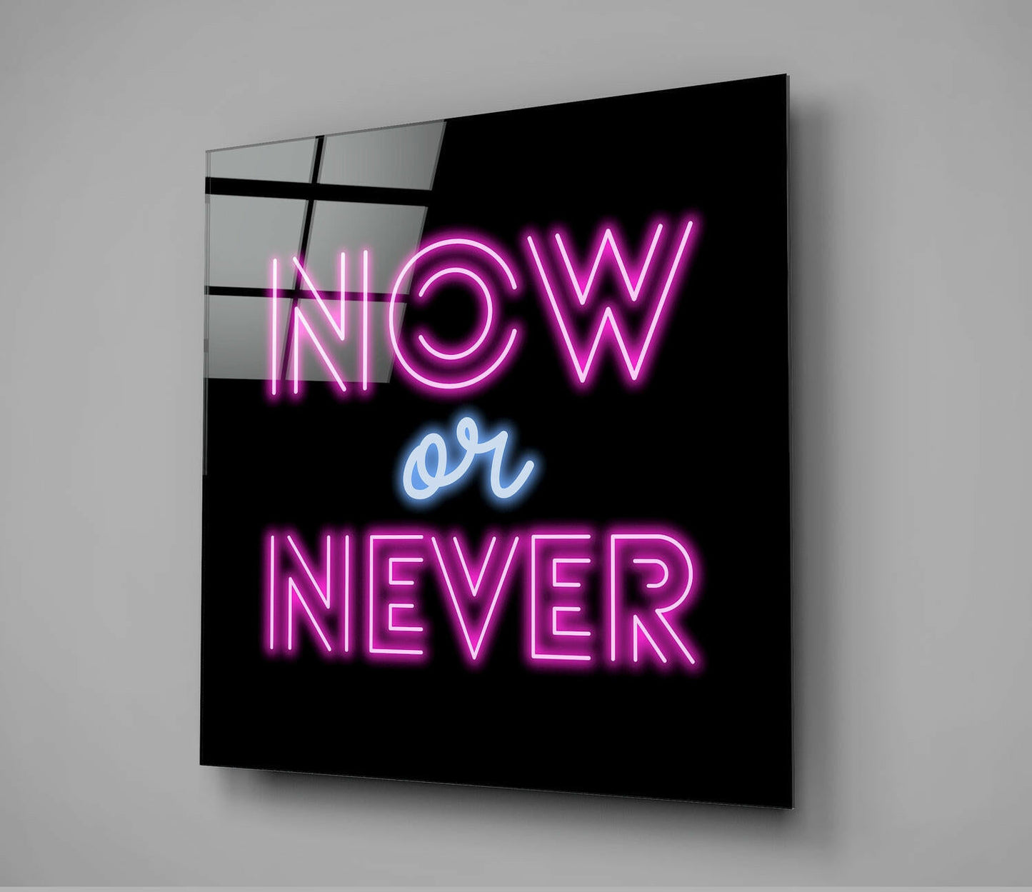 Angled view of black glass wall art with pink neon "NOW or NEVER" text and blue "or" lettering against gray background.
