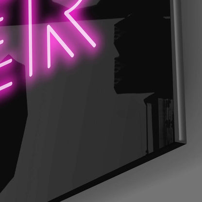 Magenta neon "Now or Never" glass wall art mounted on dark wall, angled side view showing glowing tubes and mounting hardware.