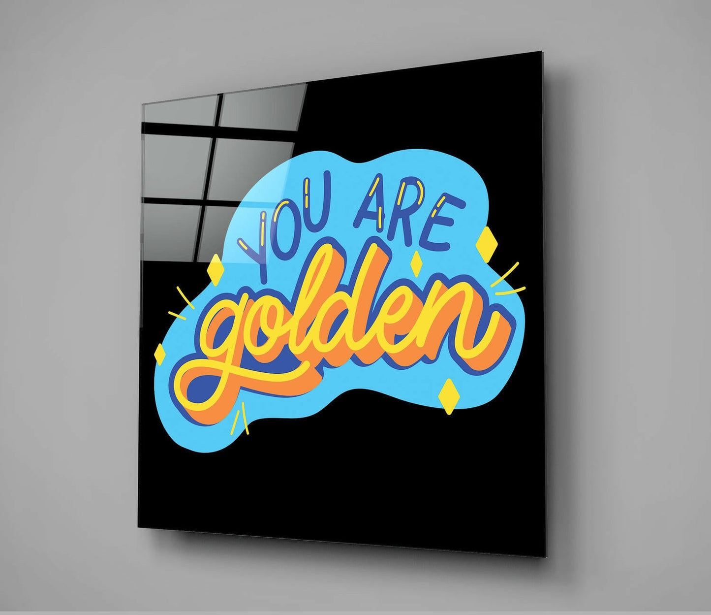 Black glass wall art panel displaying blue cloud shape with purple and gold "You Are Golden" text and yellow diamond accents, angled perspective view.