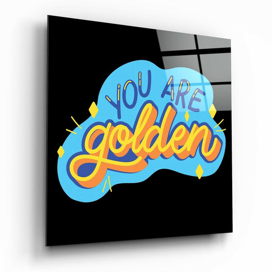 Angled perspective view of black glass wall art featuring colorful blue cloud shape with "You Are Golden" text in yellow and orange lettering with decorative yellow diamond accents.