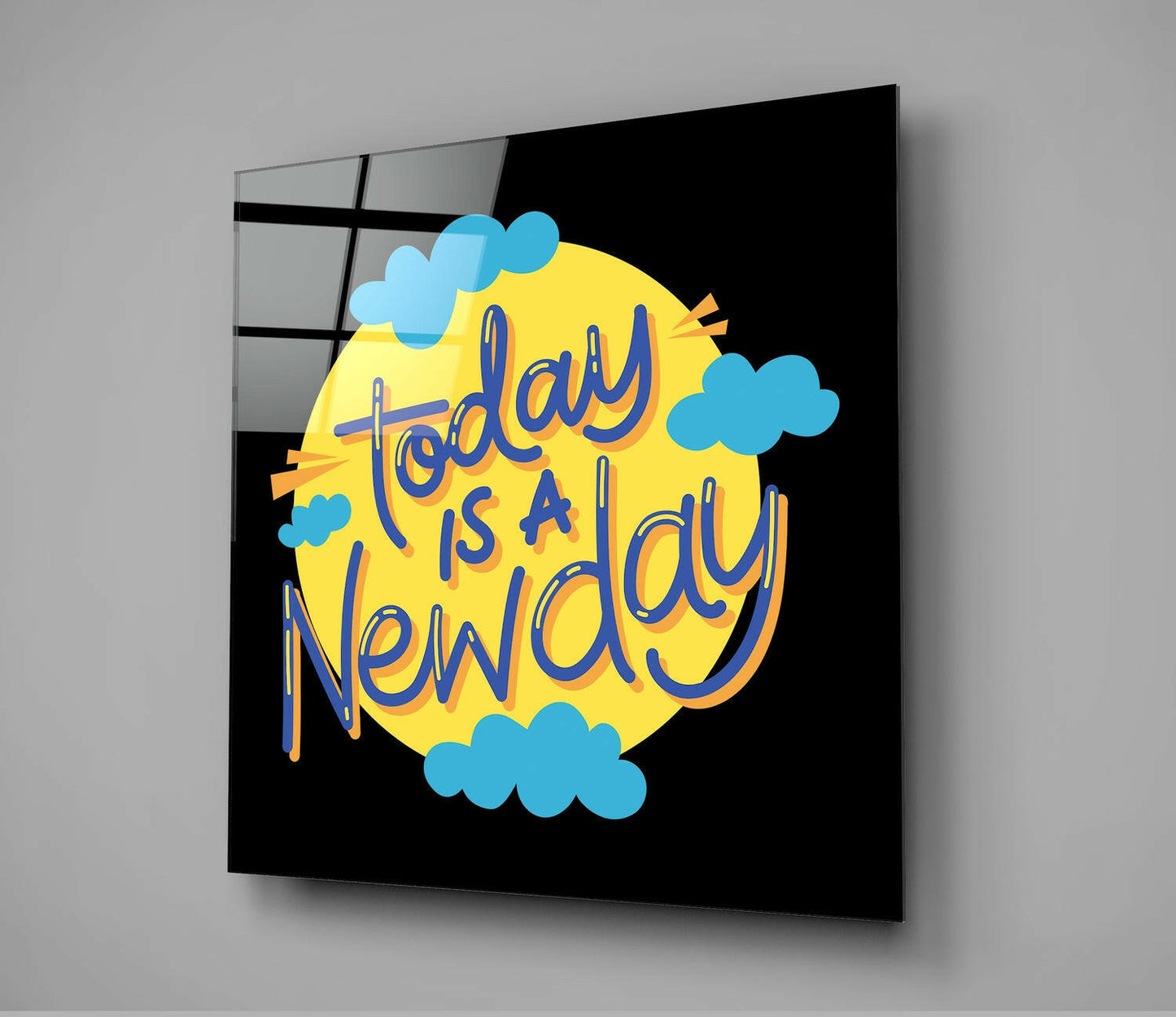 Glass wall art panel displaying "Today is a New Day" text in blue lettering on yellow circular background with blue clouds against black.