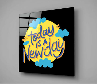 Glass wall art panel displaying "Today is a New Day" text in blue lettering on yellow circular background with blue clouds against black.