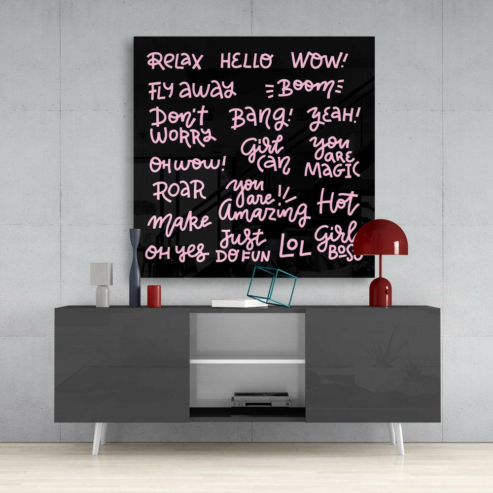 Black glass wall art with pink handwritten-style text displaying motivational phrases mounted above a gray media console with white legs.