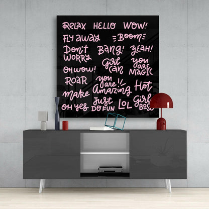 Black glass wall art with pink handwritten-style text displaying motivational phrases mounted above a gray media console with white legs.