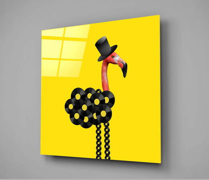 A glass wall art panel displaying a stylized red flamingo wearing a black top hat against a bright yellow background, with black vinyl record decorations forming its body.