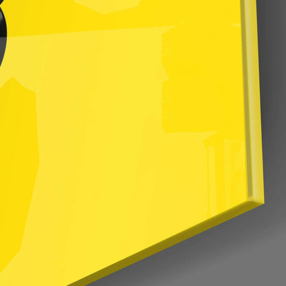 Close-up detail of bright yellow glass wall art edge showing thickness and glossy surface against gray background.