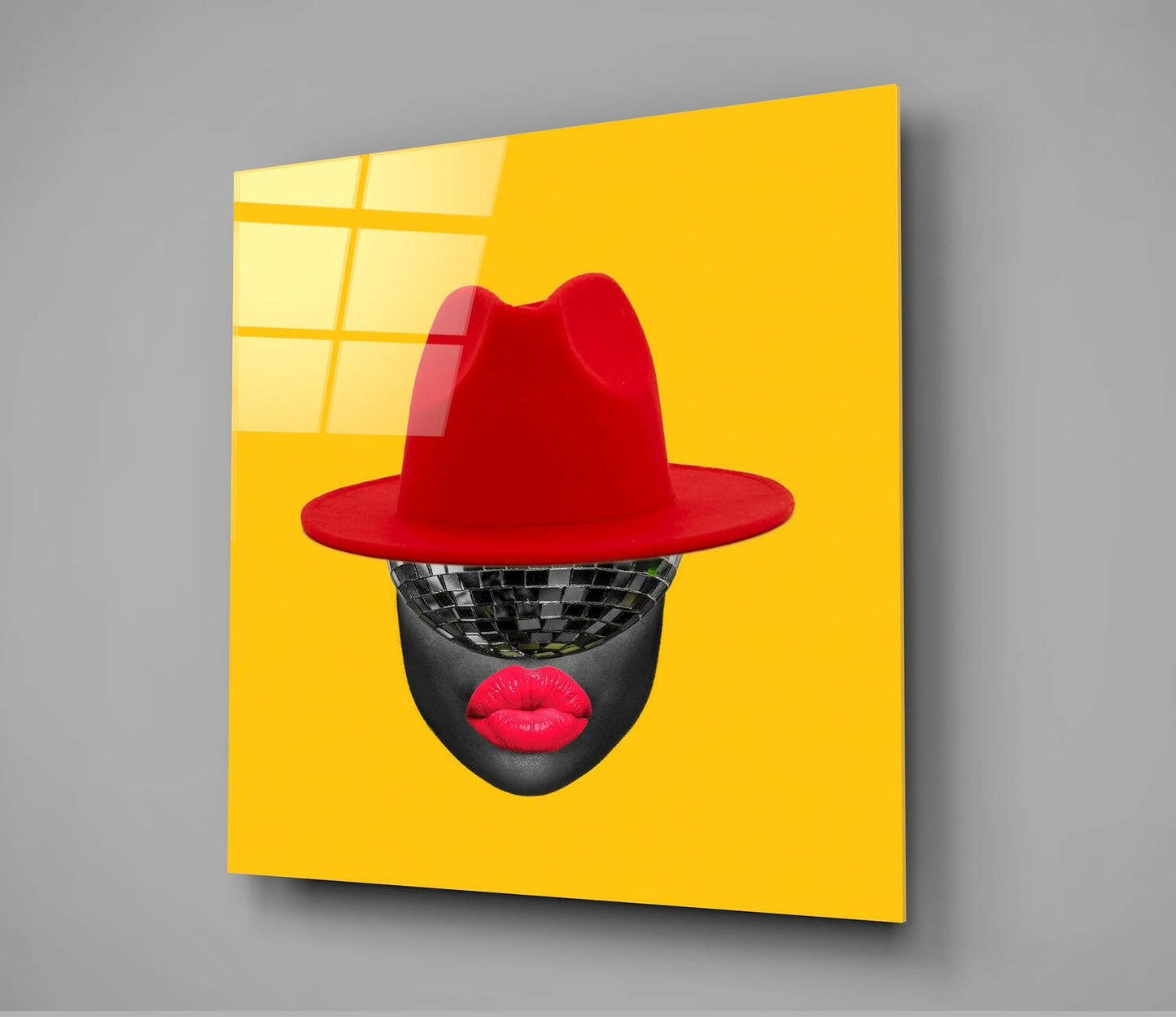 Angled view of bright yellow glass wall art featuring a stylized face with disco ball eyes, red lips, and red fedora hat.