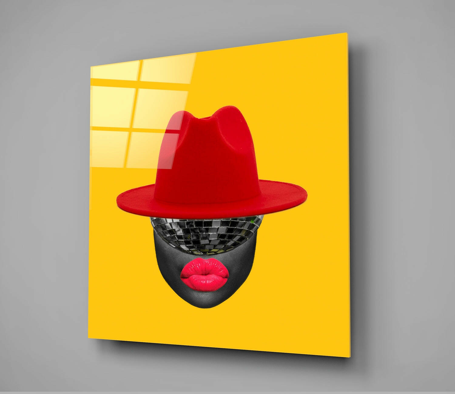 Angled view of bright yellow glass wall art featuring a stylized face with disco ball eyes, red lips, and red fedora hat.