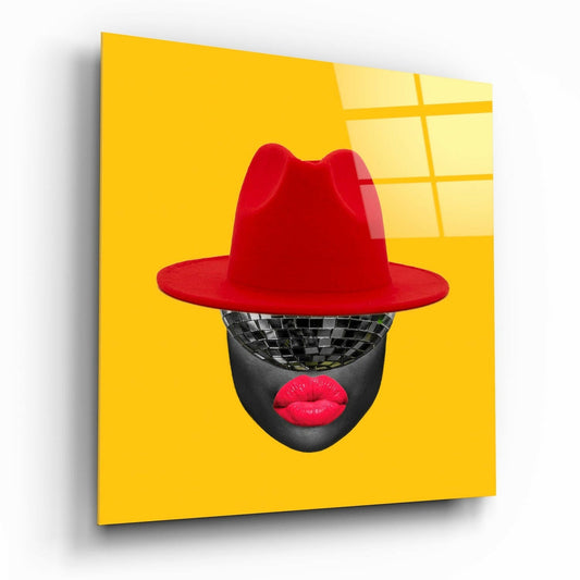 Black disco ball head wearing bright red fedora hat and red lips against vibrant yellow background on glass wall art.