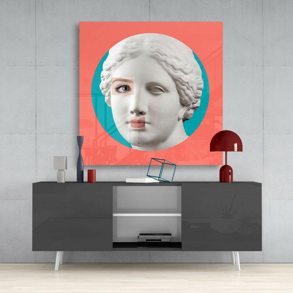 Modern interior display showing coral and teal glass wall art of classical female head sculpture mounted above dark gray console table with decorative accessories.