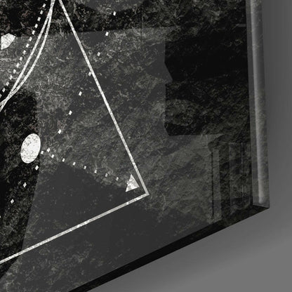 Close-up overhead view of triangular glass wall art with white geometric lines and calibration markers on textured dark background.