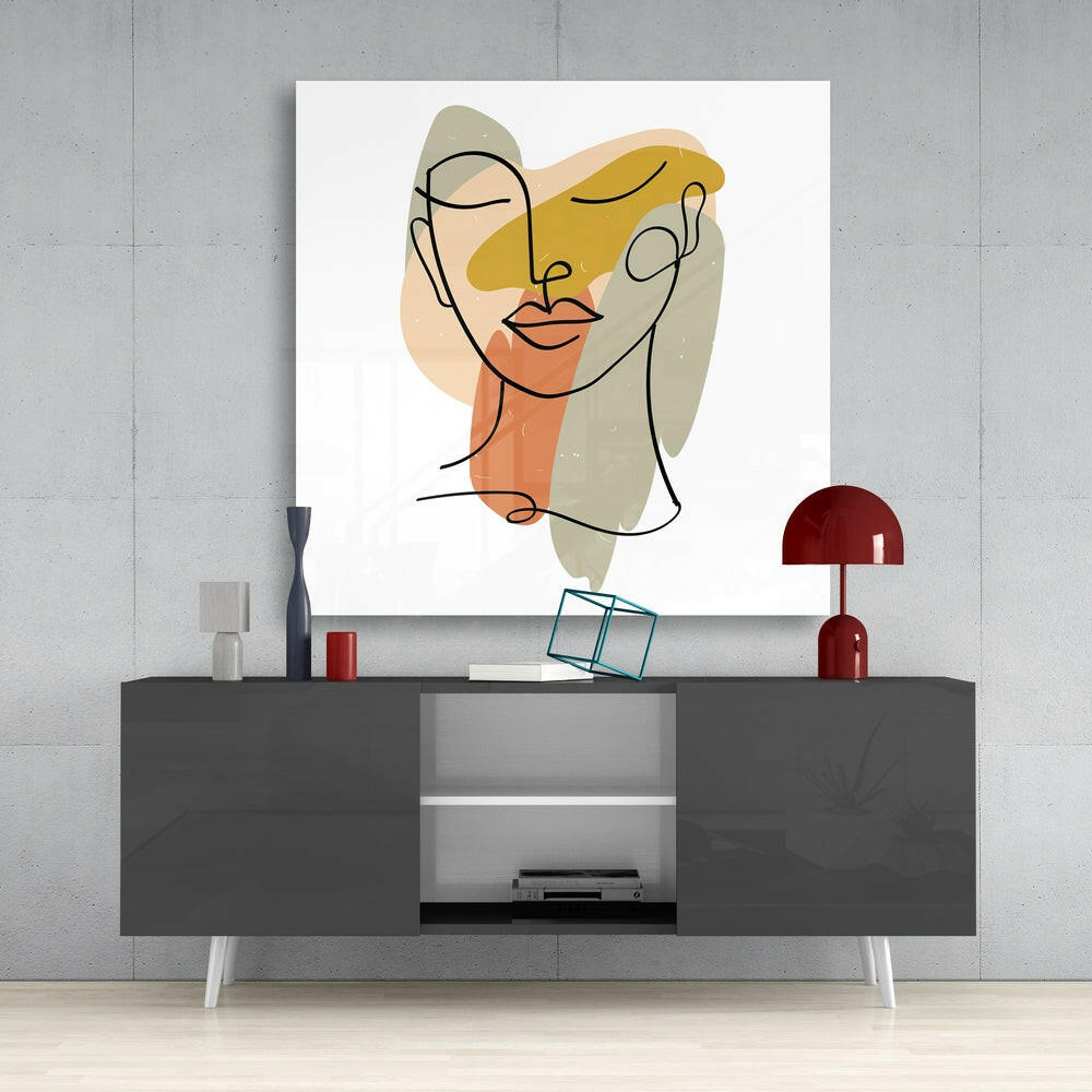 Abstract line-drawn face with yellow, orange, and beige watercolor shapes displayed above modern gray console table with red lamp.