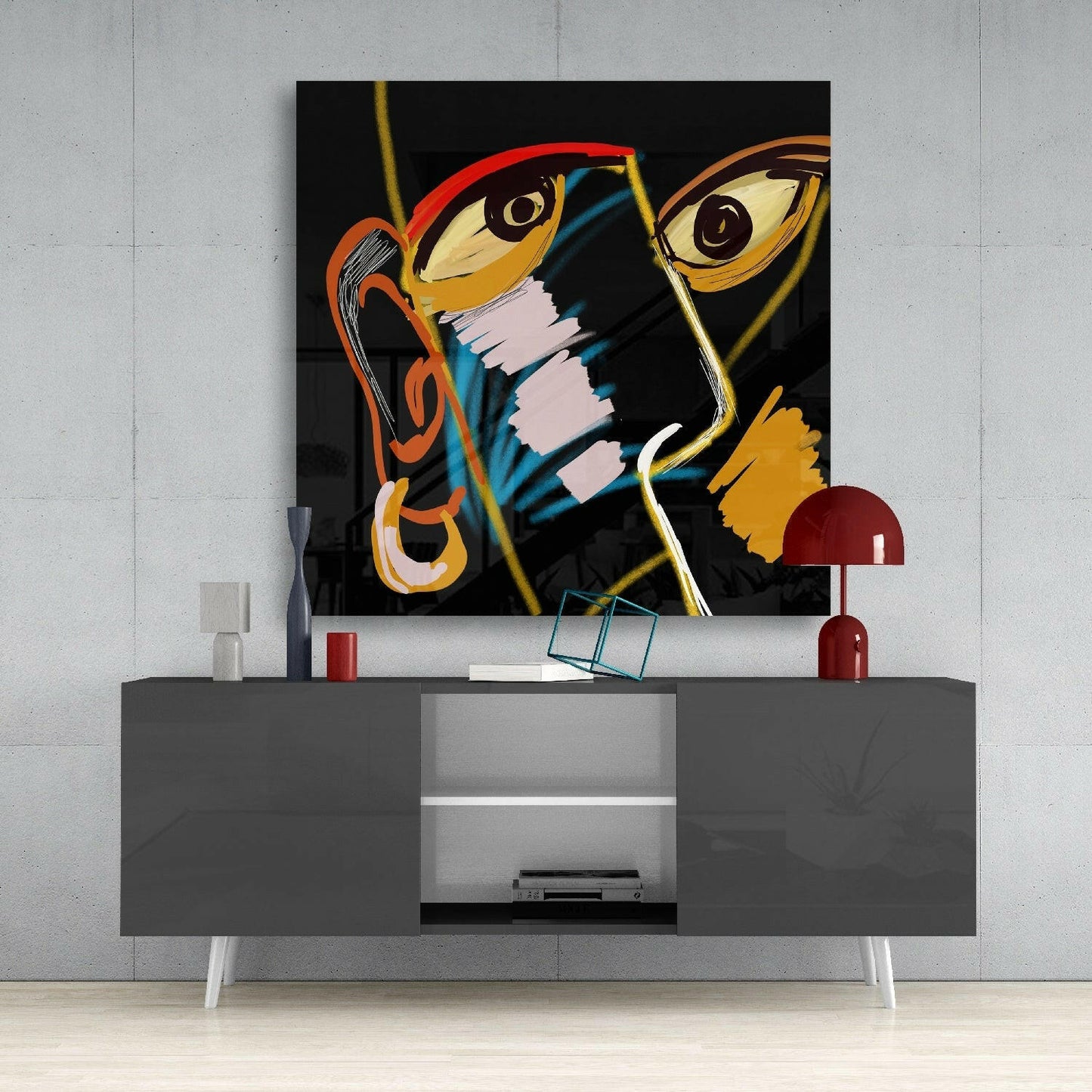 Bold abstract artwork with stylized faces in red, orange, yellow, and blue on black glass canvas displayed above gray media console with red lamp.