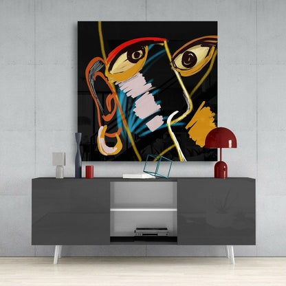 Bold abstract artwork with stylized faces in red, orange, yellow, and blue on black glass canvas displayed above gray media console with red lamp.
