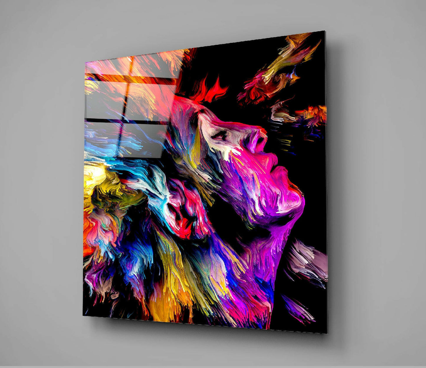 Colorful Dreams Glass Wall Art displayed at an angle showing vibrant abstract brushstrokes in magenta, yellow, blue, and orange on a black background.