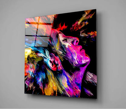 Colorful Dreams Glass Wall Art displayed at an angle showing vibrant abstract brushstrokes in magenta, yellow, blue, and orange on a black background.
