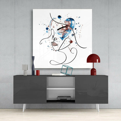 Abstract line-drawn face with blue and burgundy watercolor splashes displayed above gray media console with red lamp and accessories.