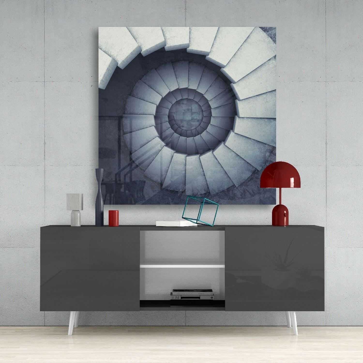Spiral staircase wall art displayed above a dark gray media console with red lamp and accessories in minimalist interior setting.