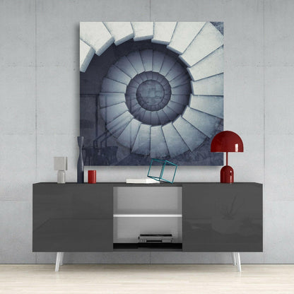 Spiral staircase wall art displayed above a dark gray media console with red lamp and accessories in minimalist interior setting.