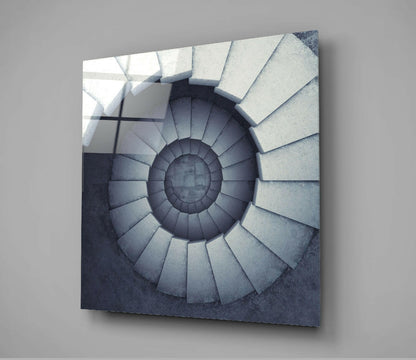 Square glass panel displaying a spiral staircase descending into shadow, rendered in grayscale tones, mounted on gray wall.