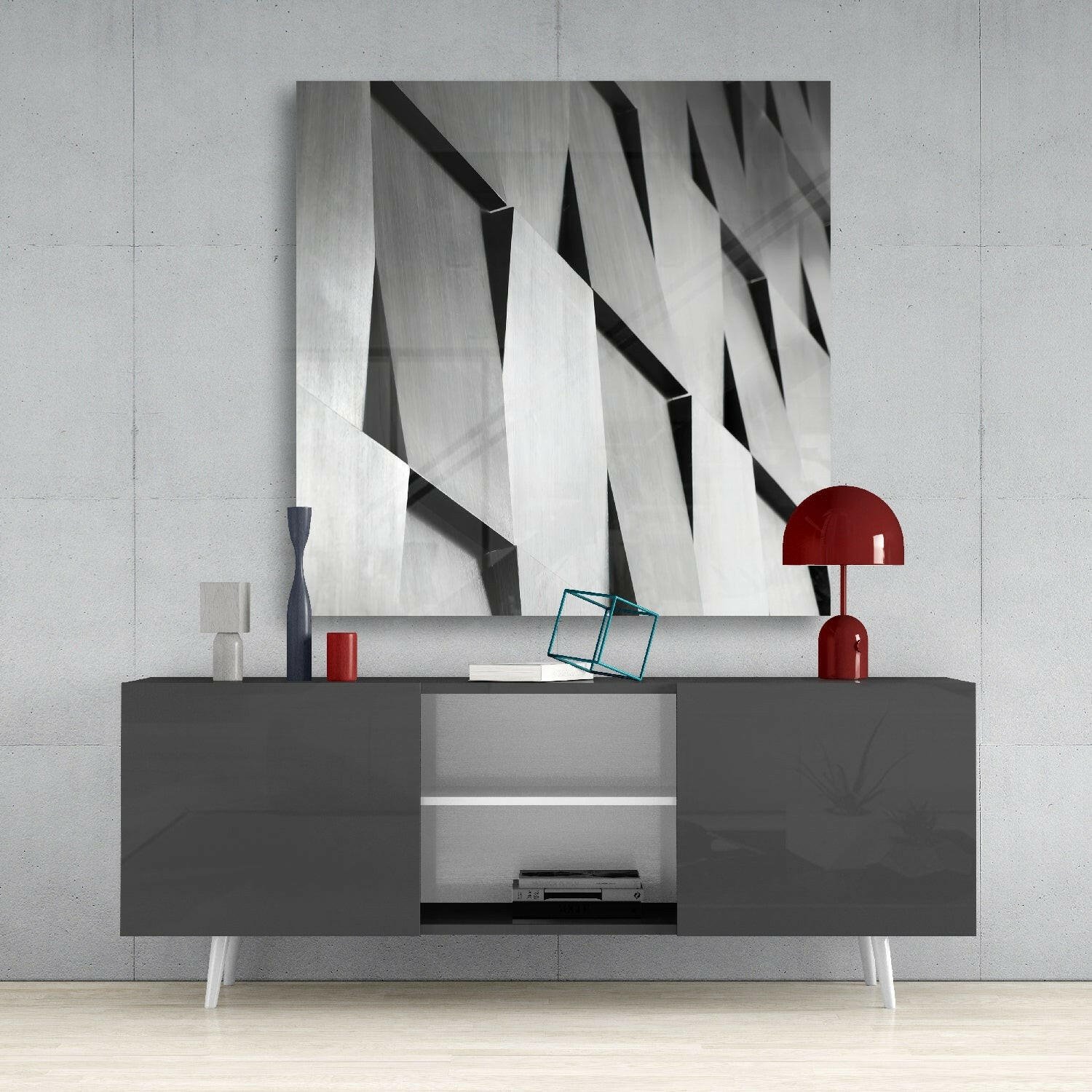 Modern glass wall art with geometric black and white abstraction displayed above gray media console with red accent lamp.