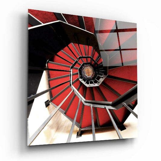 Overhead view of a red and black spiral staircase with metal railings descending toward a vanishing point, with white walls visible below.