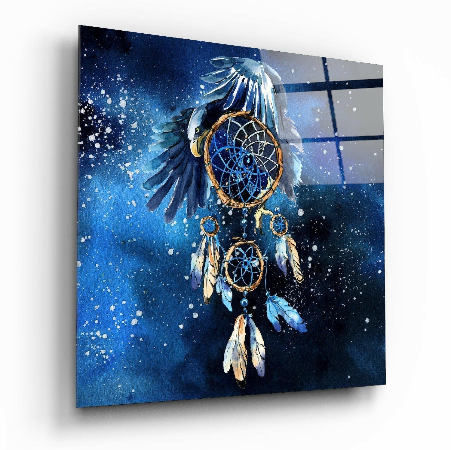 Angled view of glass wall art displaying an eagle dreamcatcher with blue feathers, golden rings, and white feathers against a deep blue splattered background.