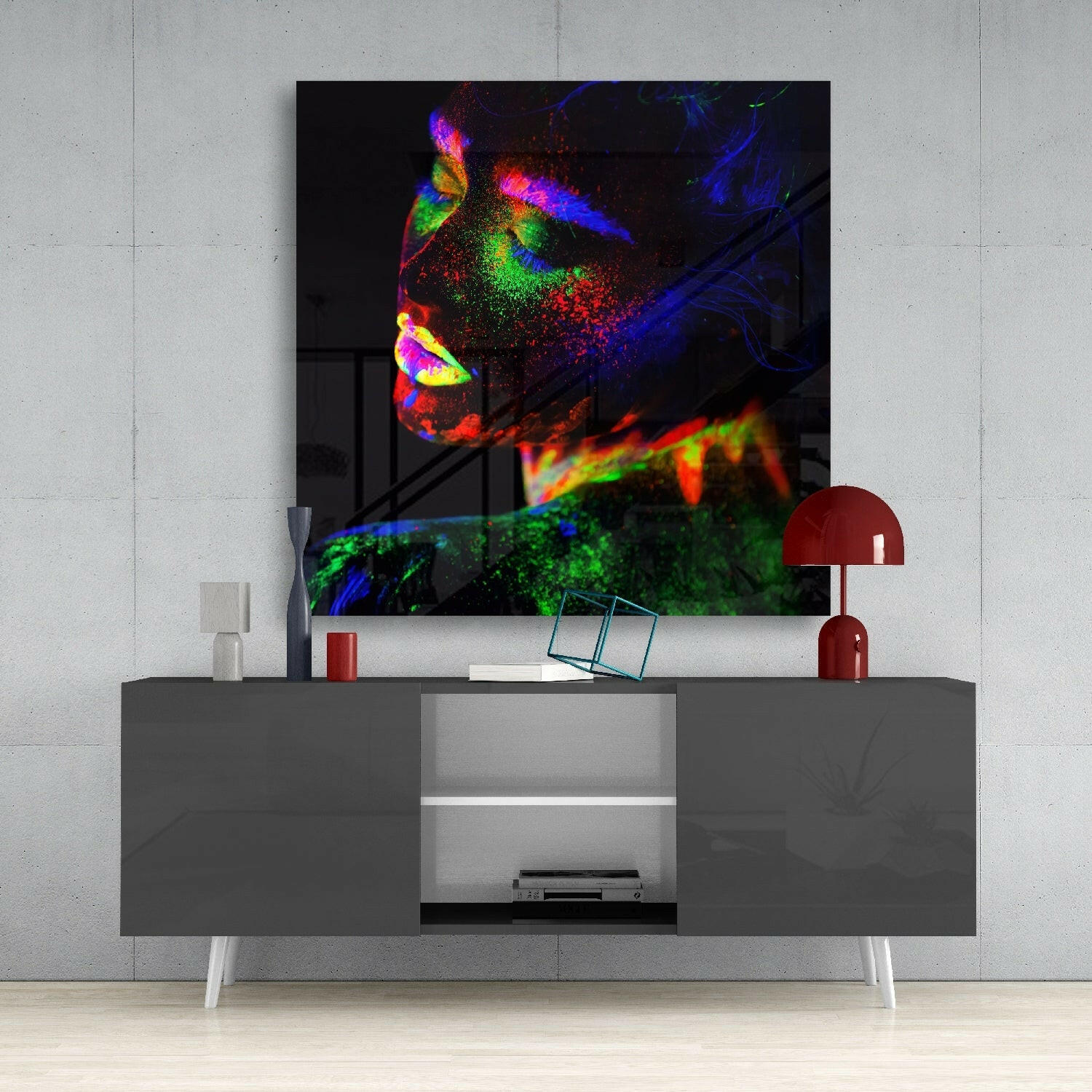 Neon color makeup glass wall art hung above gray media console with red lamp and decorative objects, showing vibrant fluorescent portrait.