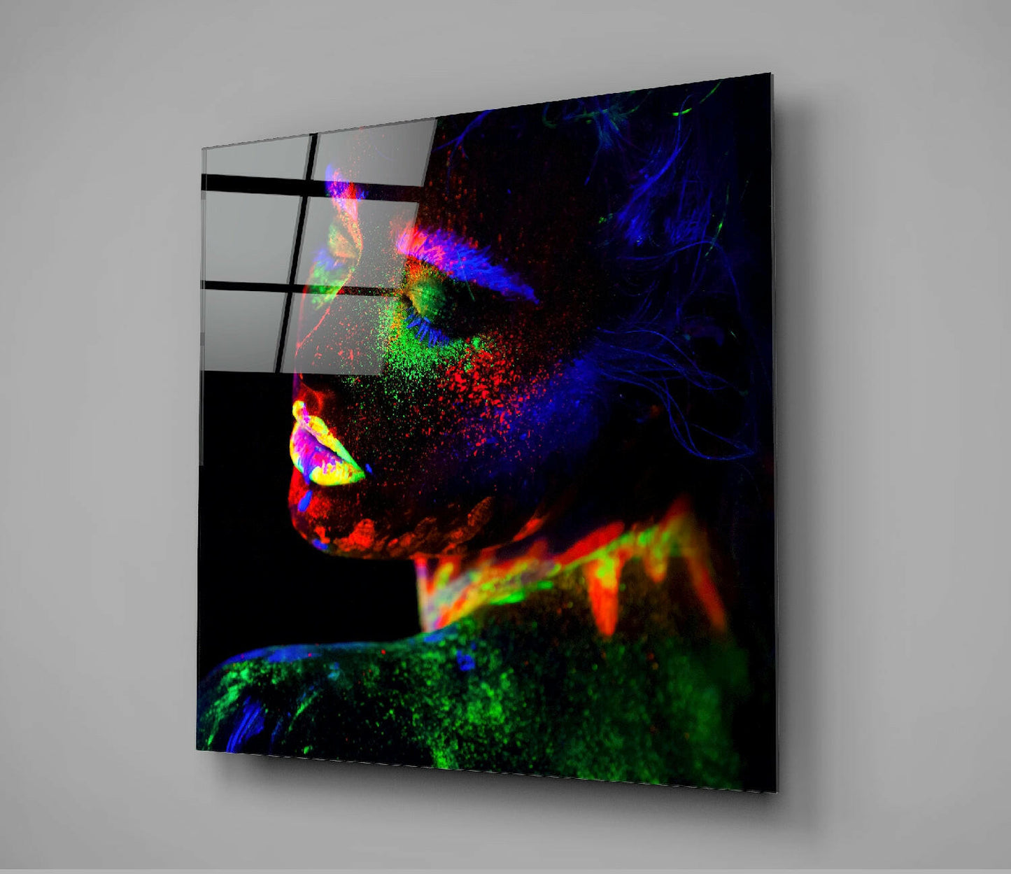 Angled view of neon color makeup glass wall art mounted on gray wall, displaying vibrant fluorescent pink, blue, green, and red pigments on black background.