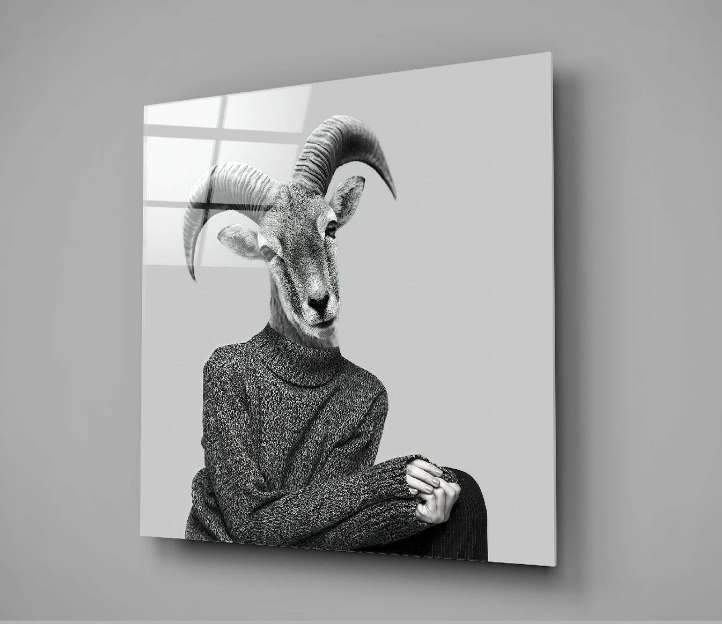 Black and white portrait of antelope head on human figure wearing gray sweater, displayed on glass panel against white wall.