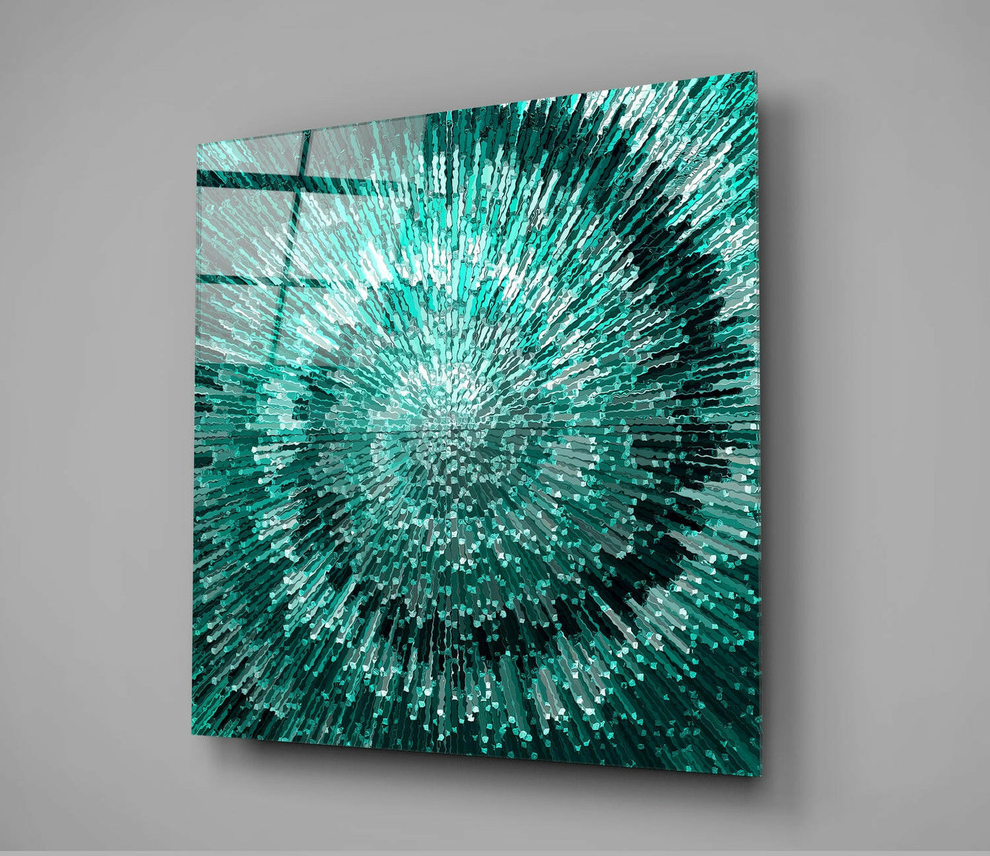 Square glass wall art with radiating teal and white rectangular pieces creating a sunburst pattern, displayed at an angle against gray background.
