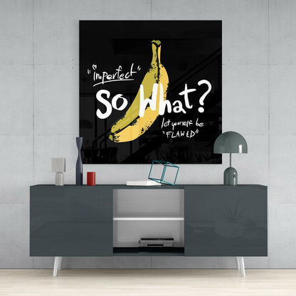 Black glass wall art with yellow banana illustration and white text reading "Imperfect" So What? let yourself be "FLAWED" displayed above gray media console.