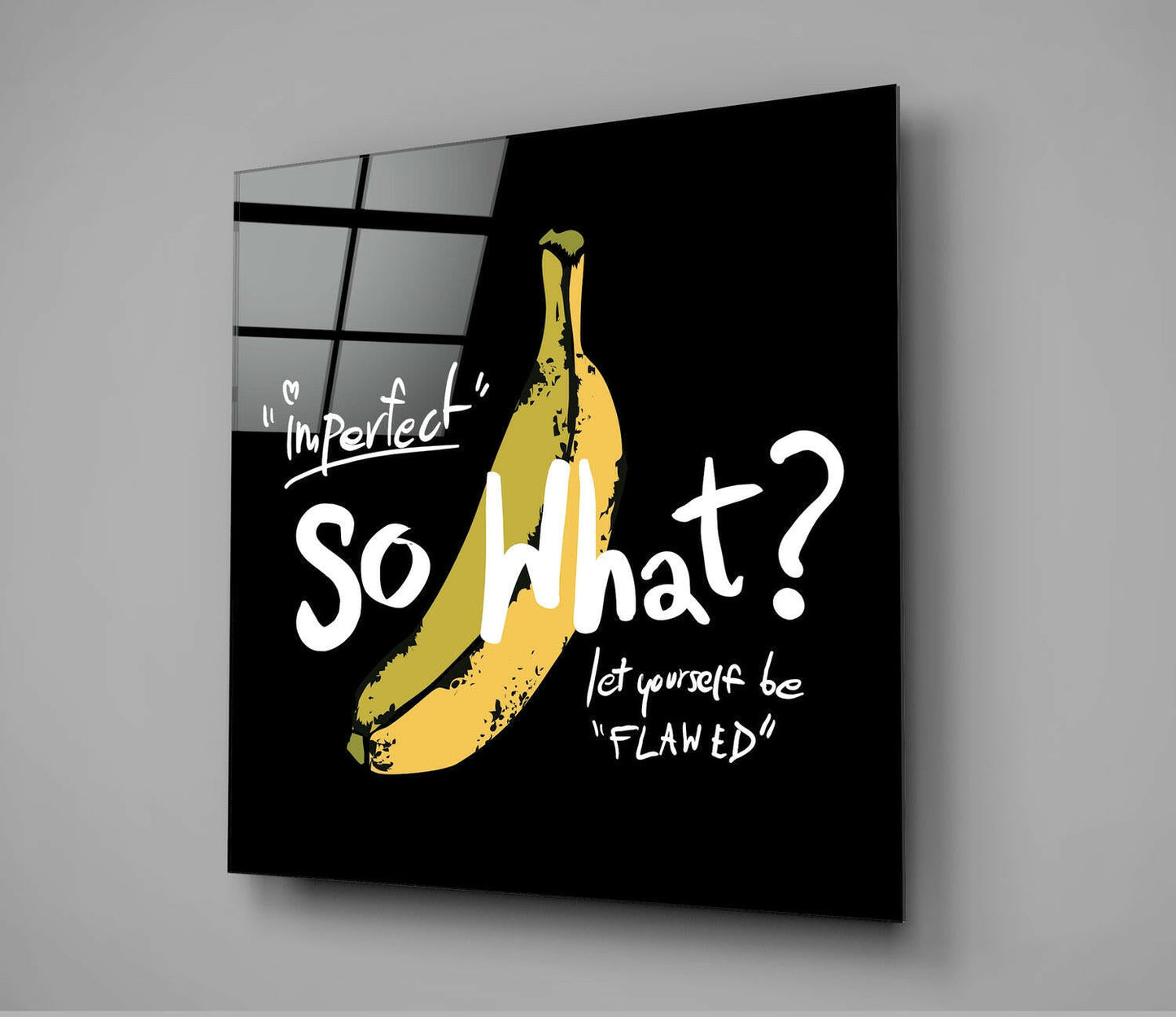 Black glass wall art with yellow banana illustration and white text reading "Imperfect" "So What?" and "let yourself be Flawed", displayed at an angle against gray background.