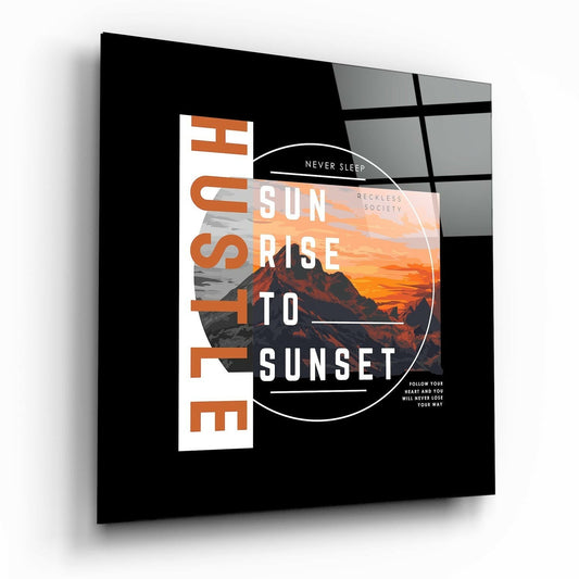 Black glass wall art panel with orange and white typography, mountain sunset photograph, and circular design element, displayed at an angle.