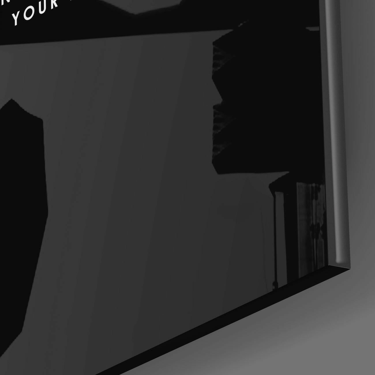Close-up side angle of black glass wall art panel showing textured surface and white edge trim against gray background.