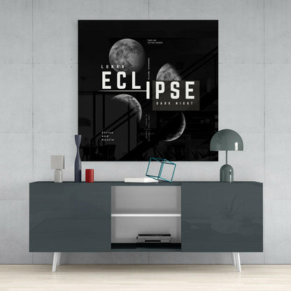 Black lunar eclipse glass wall art with white typography displayed above a dark gray dresser in a minimalist interior setting.