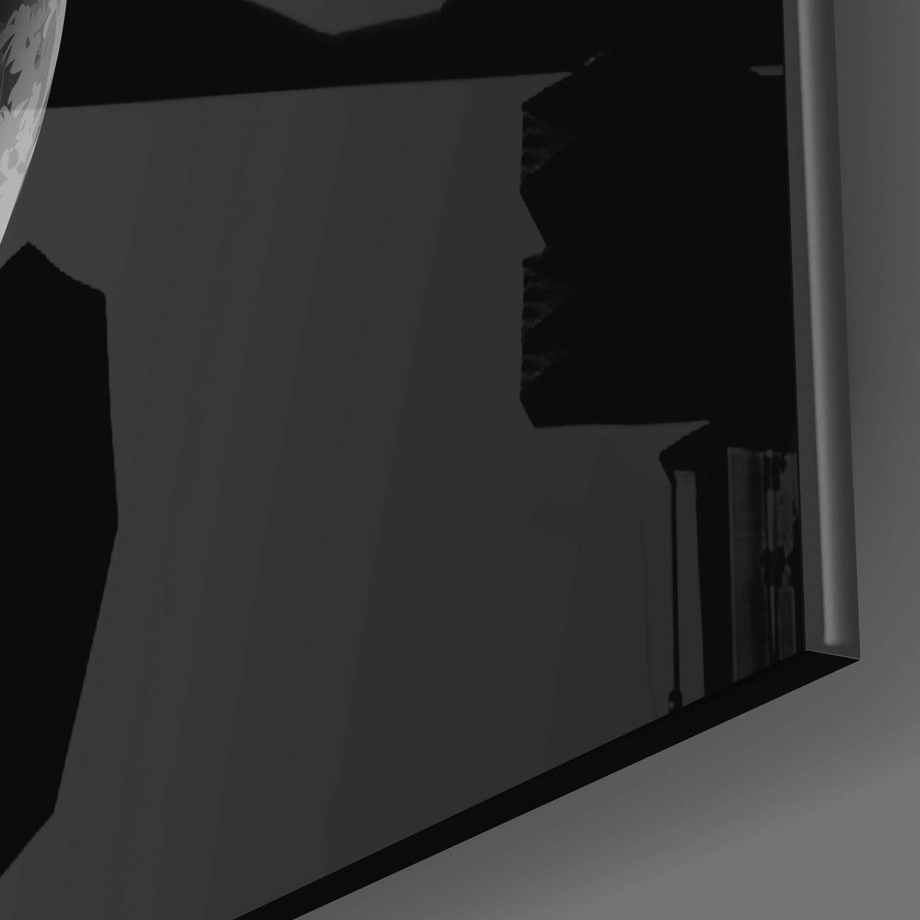 Close-up angled view of Eclipse Glass Wall Art showing dark geometric shapes against light gray background with white frame edge.