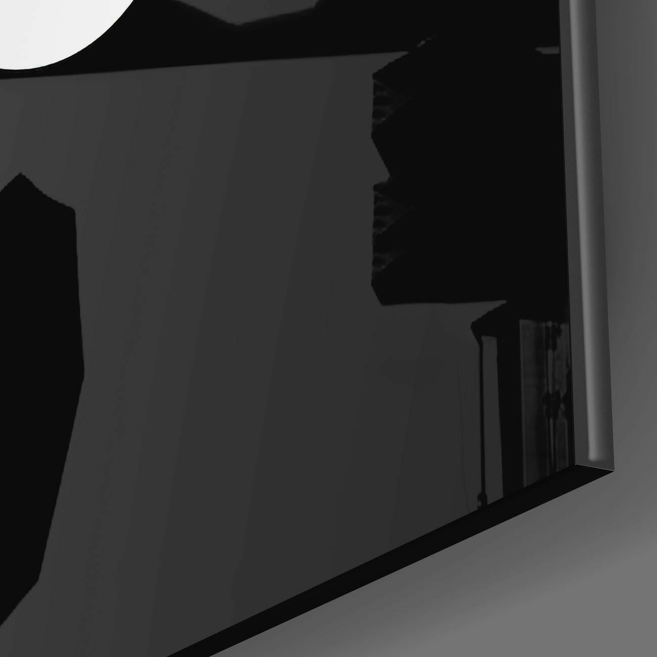 Close-up angled view of black glass wall art panel showing edge detail and surface reflection against gray background.