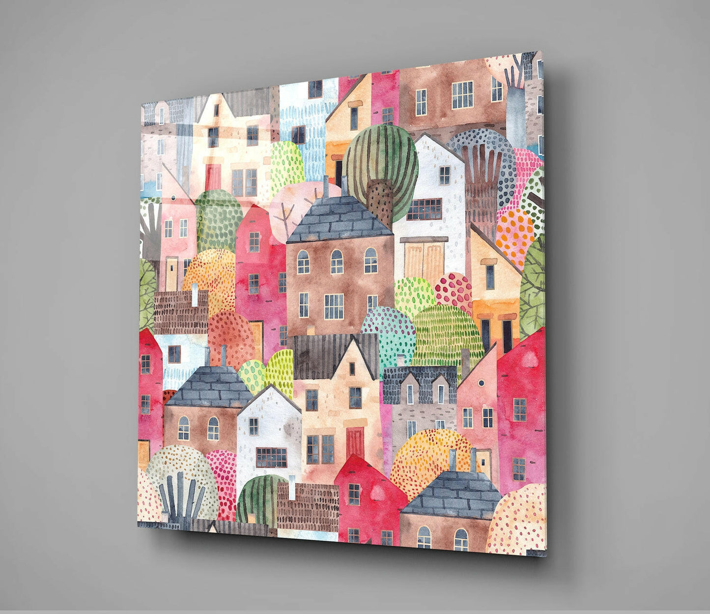 Square glass wall art panel displaying a dense, colorful illustration of overlapping houses in pink, red, brown, and cream with decorative cacti and patterned foliage, mounted on gray wall.