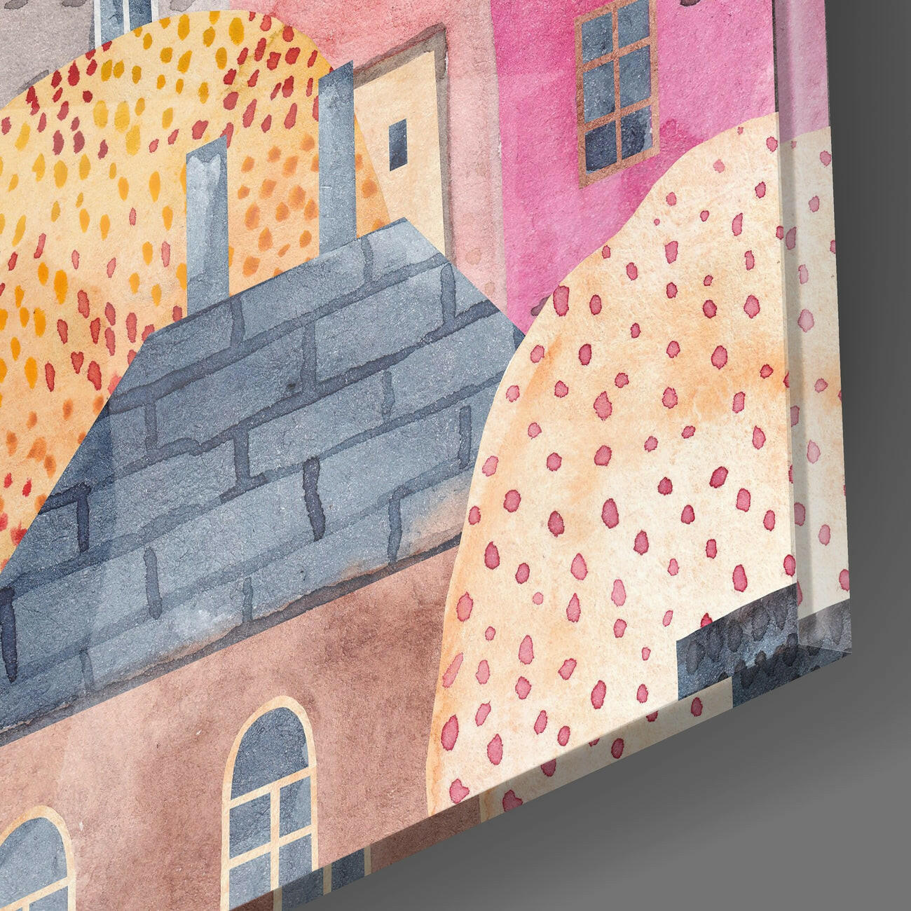 Angled view of colorful glass wall art showing painted houses with pink, yellow, and blue tones and dotted pattern details.