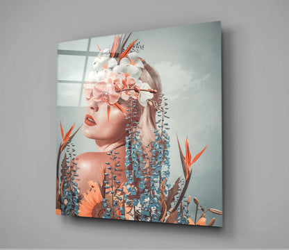 Square glass wall art displaying a woman's profile merged with orange and blue flowers against a pale blue background, mounted on gray wall.