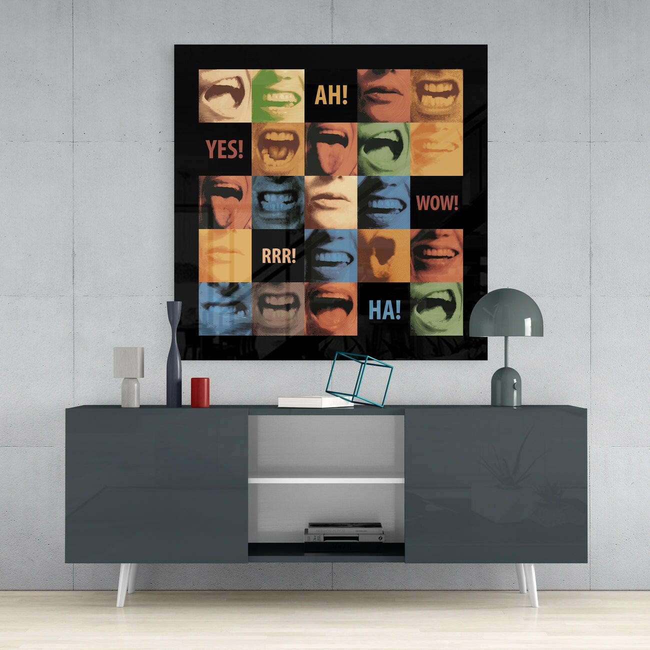 Colorful glass wall art with grid of close-up mouths and expressions displaying text "AH!", "YES!", "WOW!", "RRR!", and "HA!" mounted above a dark TV console.