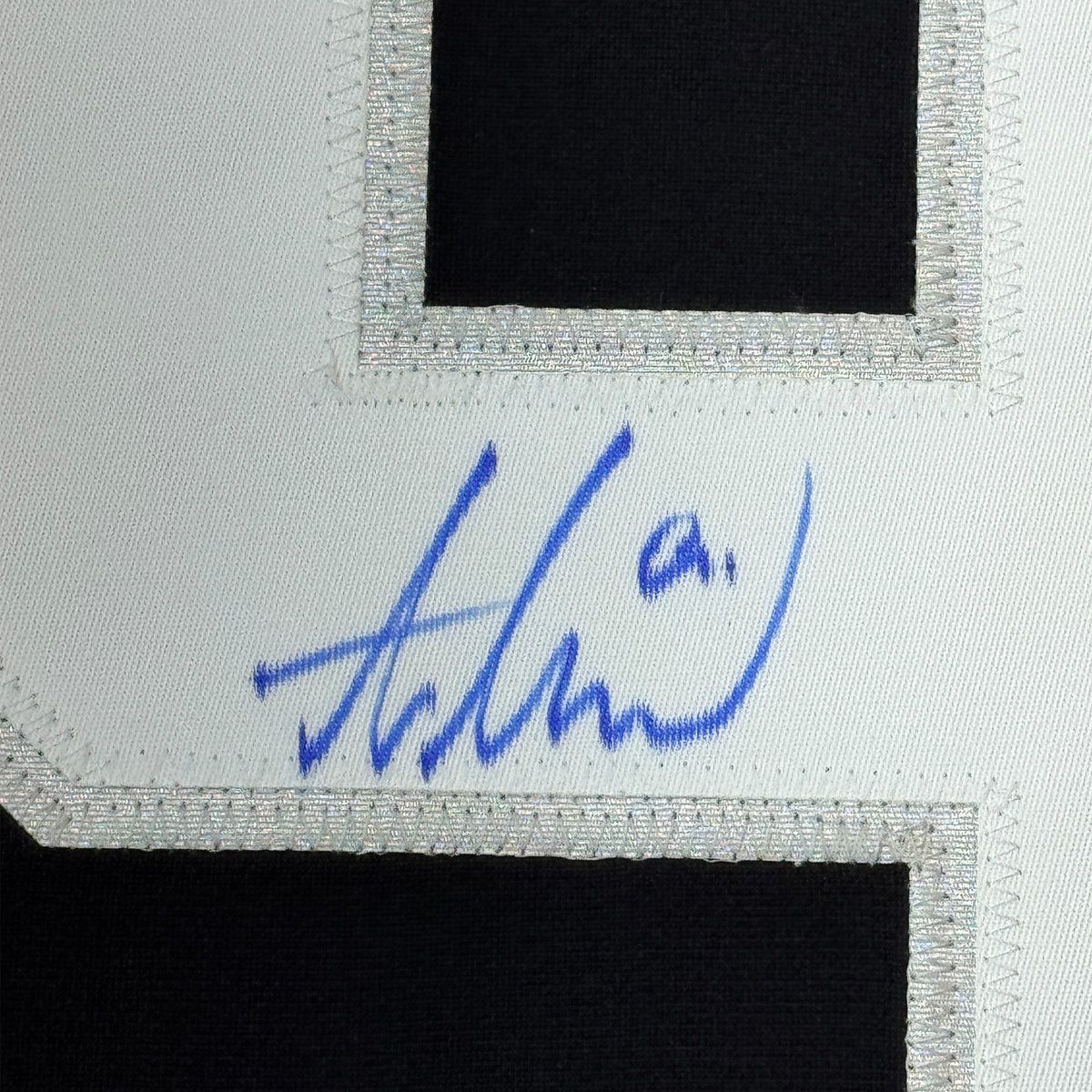 Close-up of blue autograph signature on white fabric border of black hockey jersey.