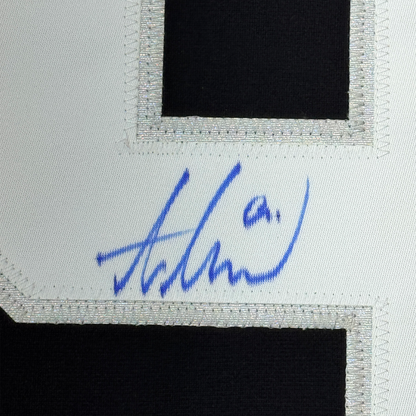Close-up of blue autograph signature on white fabric border of black hockey jersey.