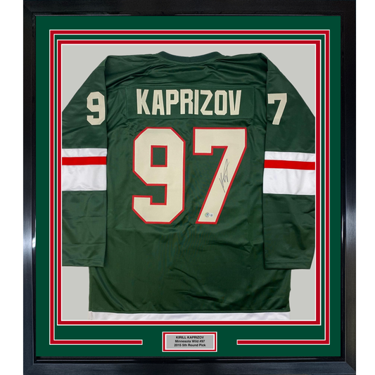 Framed green Minnesota Wild hockey jersey #97 with "KAPRIZOV" name and signature, red and white striping, displayed flat against cream backing with red border matting.