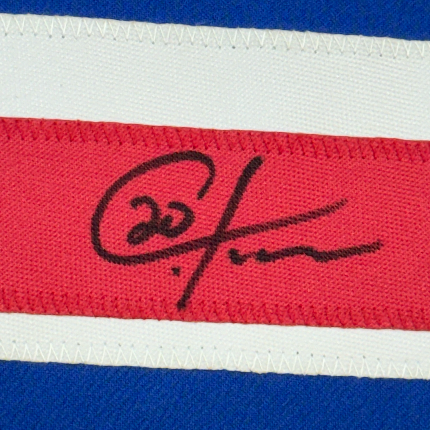 Close-up of handwritten black signature on red stripe of blue, white, and red striped fabric jersey.