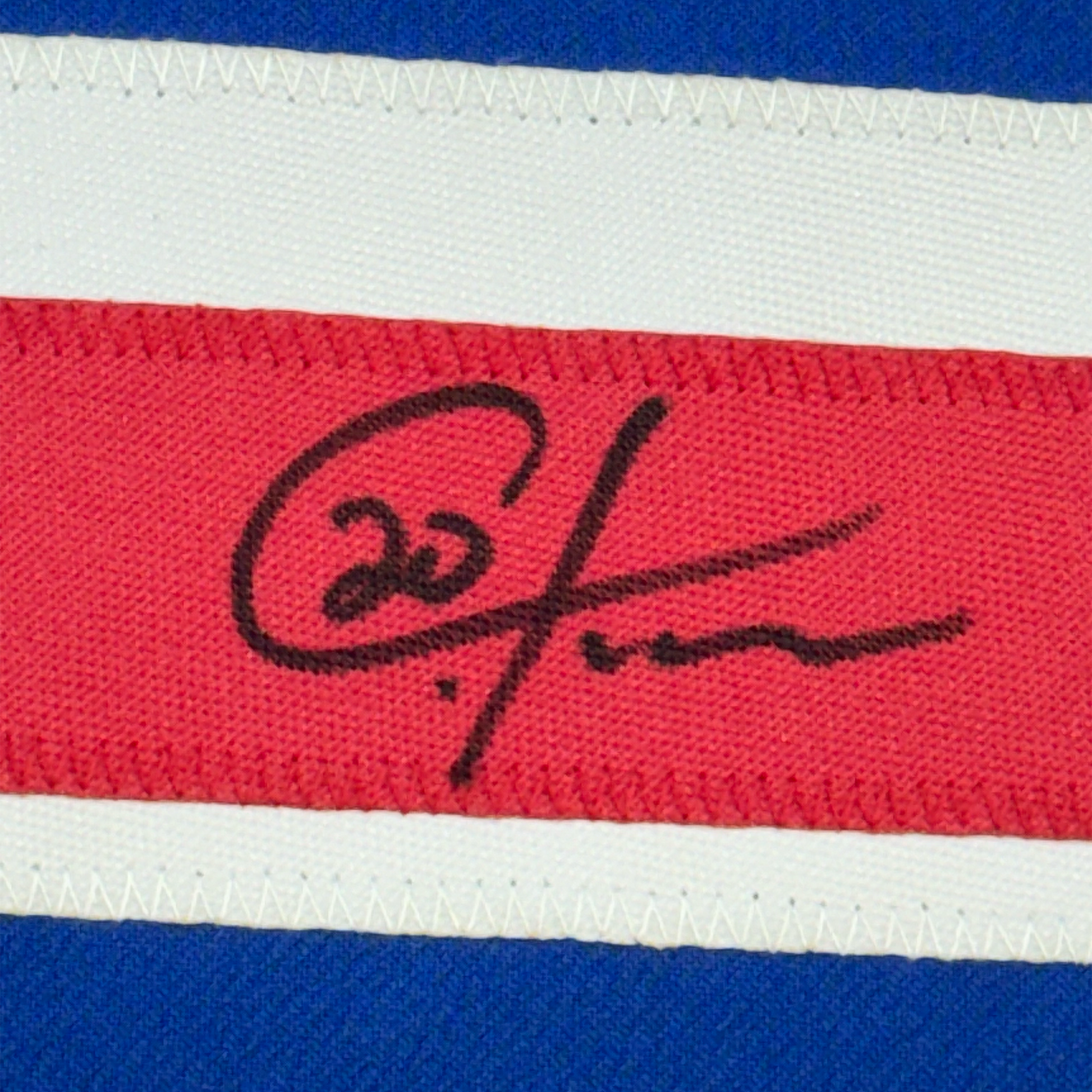 Close-up of handwritten black signature on red stripe of blue, white, and red striped fabric jersey.