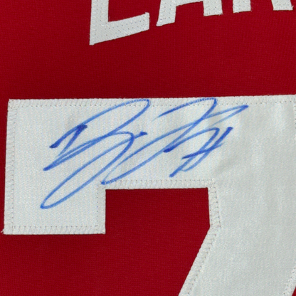 Close-up of blue autographed signature on white nameplate strip of red hockey jersey.