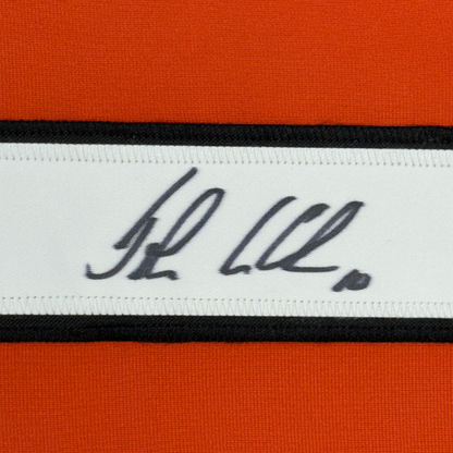 Close-up of autographed nameplate on white ribbon band showing handwritten "JL 22" signature in dark ink between orange and black fabric stripes.